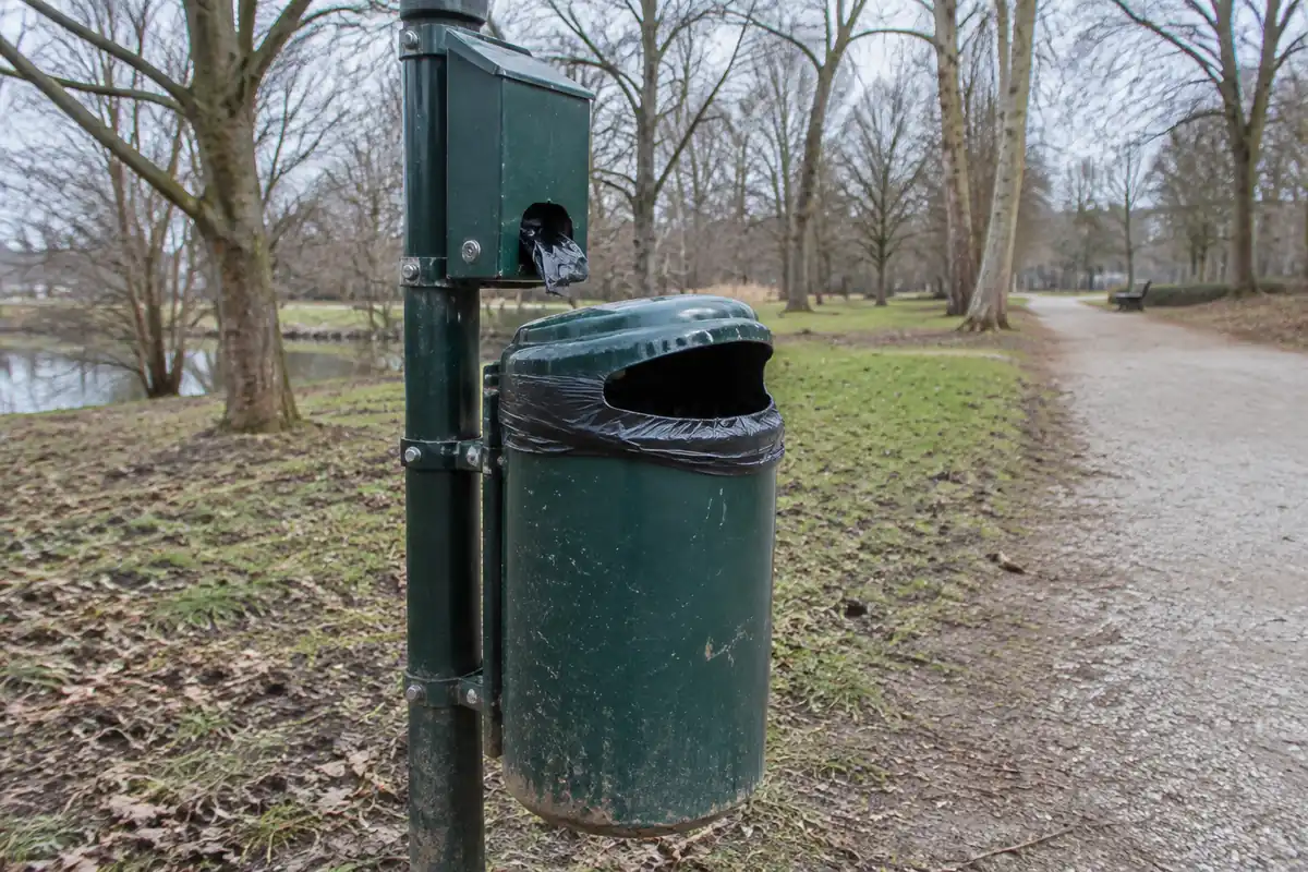 Corbeille de rue verte avec un distributeur de sacs fixé sur son poteau, au bord d'un chemin de parc